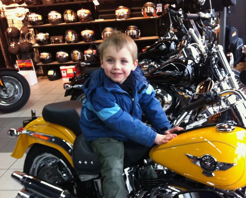 Gabriel enfant, assis sur une moto jaune dans un magasin de motos