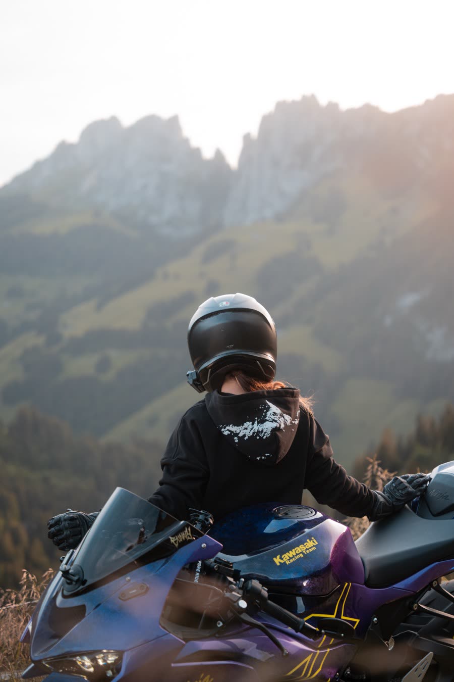 Pilote assis sur sa moto face aux montagnes, à la golden hour.